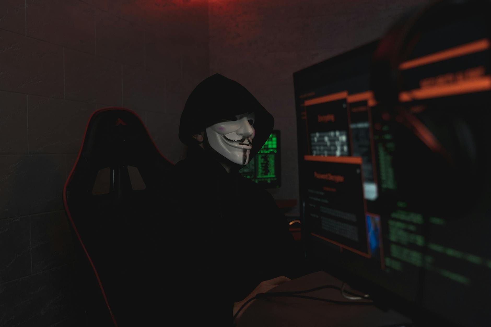 Anonimowy haker w masce pracuje przy komputerze w ciemnym pokoju