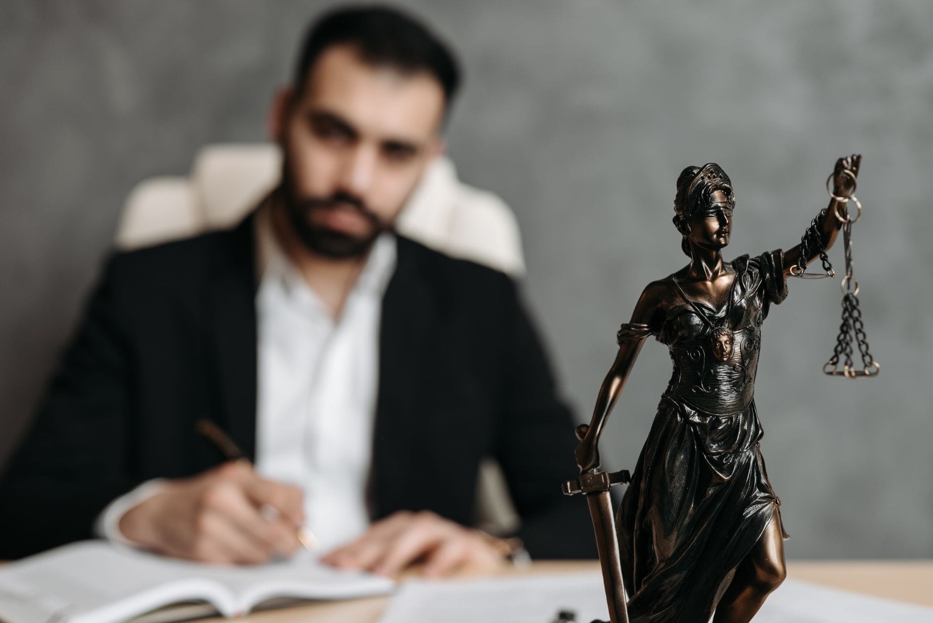 Prawnik przy biurku piszący dokument, obok statuetka Temidy Prawnik przy biurku piszący dokument, obok statuetka Temidy