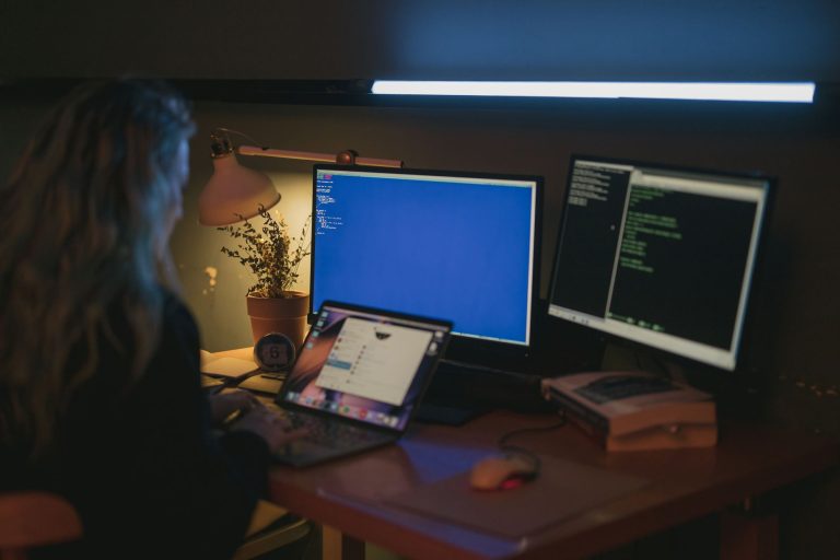 Kobieta pracująca przy wielu monitorach w domowym biurze cyberbezpieczeństwa